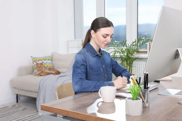 Woman working at desk and cat lying on sofa in room. Home office