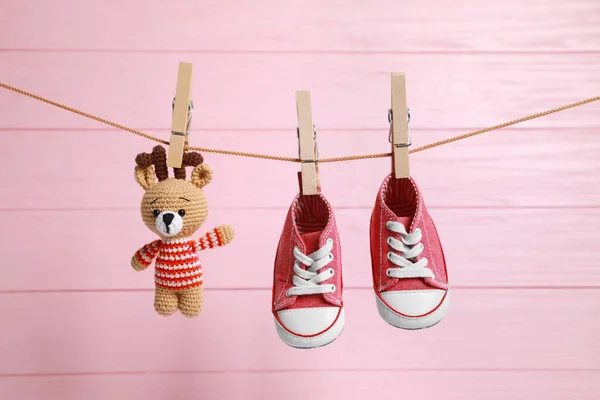 Cute baby sneakers and crochet toy drying on washing line against pink wooden wall