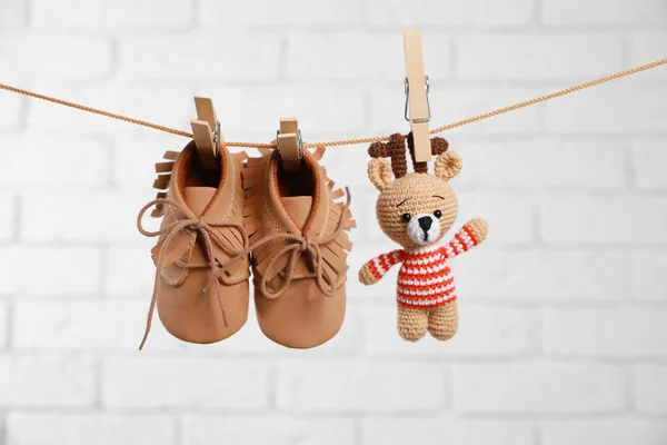 在白砖墙上的洗衣线上擦干可爱的婴儿鞋和钩针玩具 — 图库照片