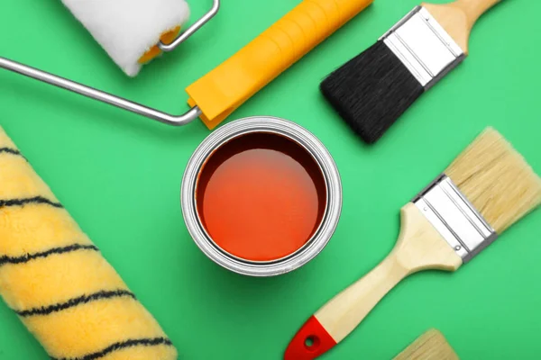 Can of orange paint, brushes and rollers on green background, flat lay