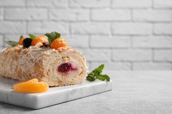 Tasty meringue roll with jam, tangerine slices and mint leaves on grey table, closeup. Space for text
