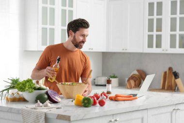 Adam mutfakta dizüstü bilgisayarla yemek pişirirken yemek yapıyor.