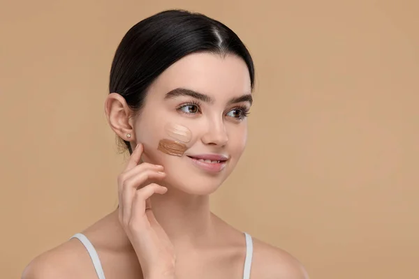 Teenage girl with swatches of foundation on face against beige background. Space for text