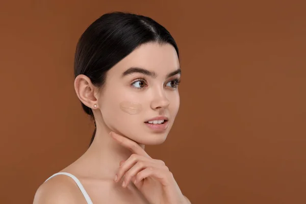 Teenage girl with swatch of foundation on face against brown background. Space for text