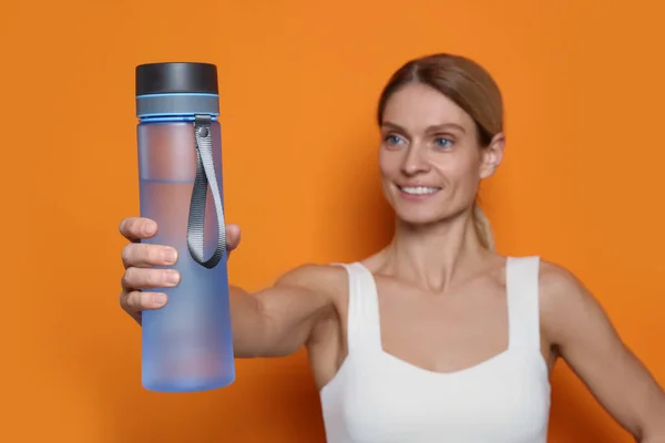 オレンジの背景に水のボトルを持つスポーツ女性 — ストック写真