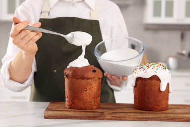 Woman decorating traditional Easter cake with glaze at white marble table in kitchen, closeup