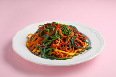 Pembe arka planda farklı renklerde spagetti tabağı.