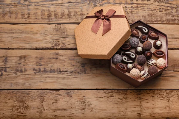 Open box of delicious chocolate candies on wooden table, top view, Space for text