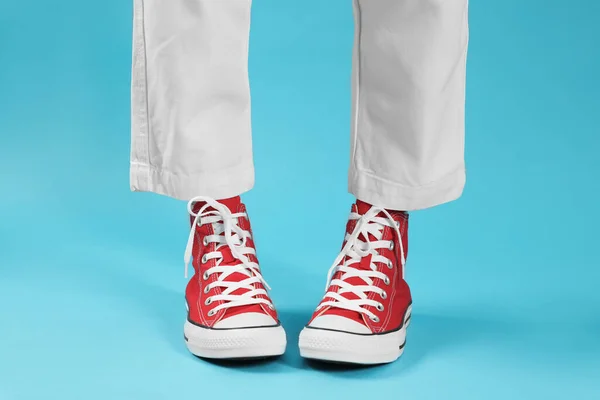 Woman in stylish gumshoes on light blue background, closeup