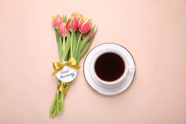Cup of coffee, beautiful tulips and card with text Good Morning on beige background, flat lay