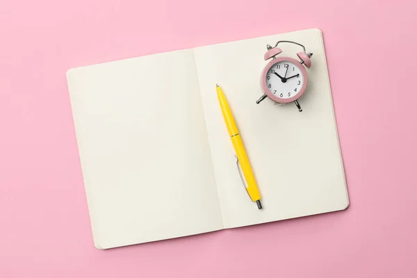 粉红背景的圆珠笔 笔记本和闹钟 顶视图 — 图库照片