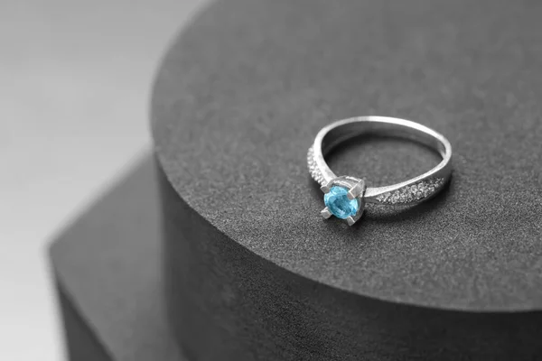 Beautiful ring with light blue gemstone on black podium, space for text. Luxury jewelry