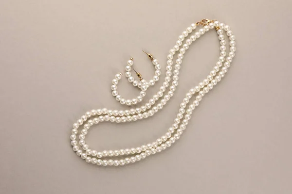 Elegant pearl necklace and earrings on beige background, top view