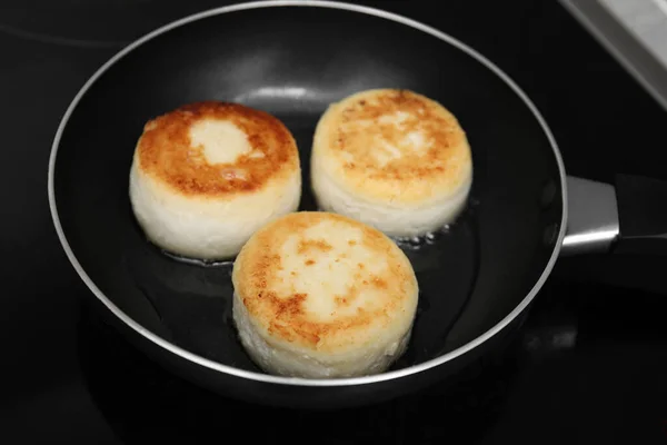 stock image Delicious cottage cheese pancakes in frying pan on cooktop, closeup