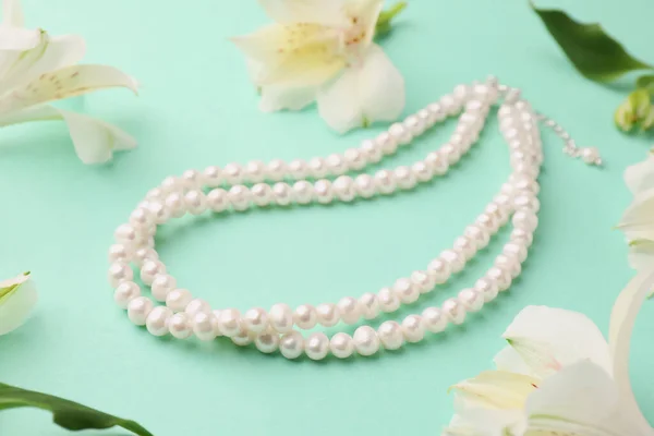 Elegant pearl necklace and beautiful flowers on turquoise background
