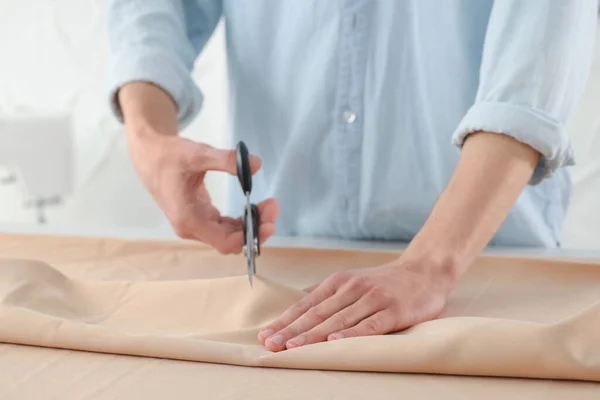 stock image Dressmaker cutting fabric with scissors at table in atelier, closeup