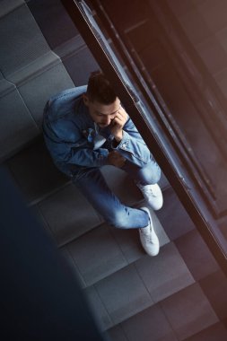 İçerideki merdivenlerde oturan üzgün adam, üst manzara. Yalnızlık kavramı