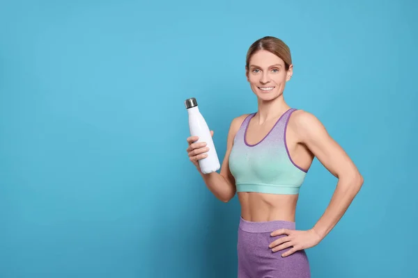 Sportswoman with thermo bottle on light blue background, space for text