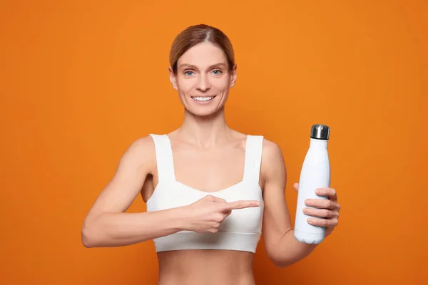 オレンジ色の背景に魔法瓶付きスポーツ女性 — ストック写真