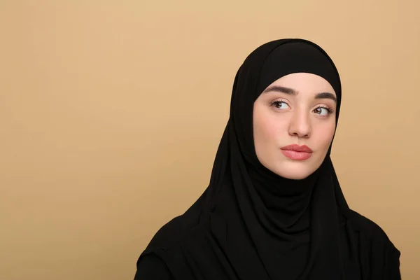 Portrait of Muslim woman in hijab on beige background, space for text