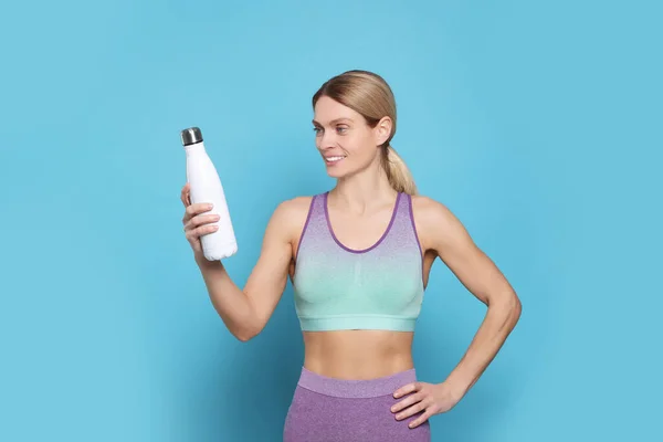 Sportswoman with thermo bottle on light blue background