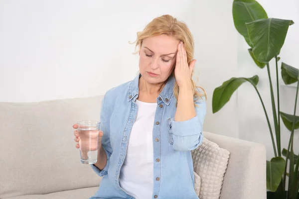 自宅のソファで頭痛に苦しんで水のガラスを持つ女性 ホルモン障害 — ストック写真