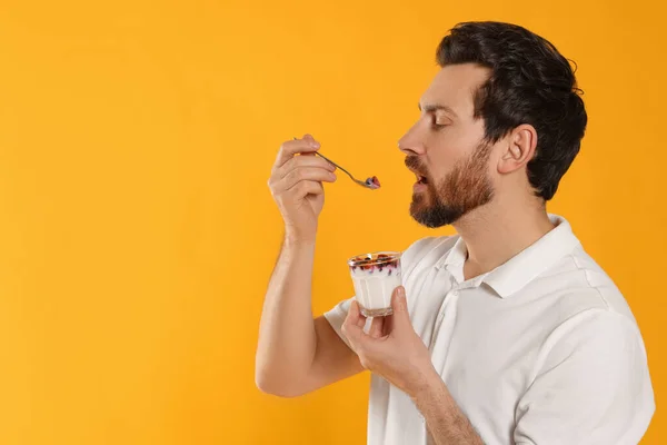 英俊的男人在黄色背景下吃美味的酸奶 案文的篇幅 — 图库照片