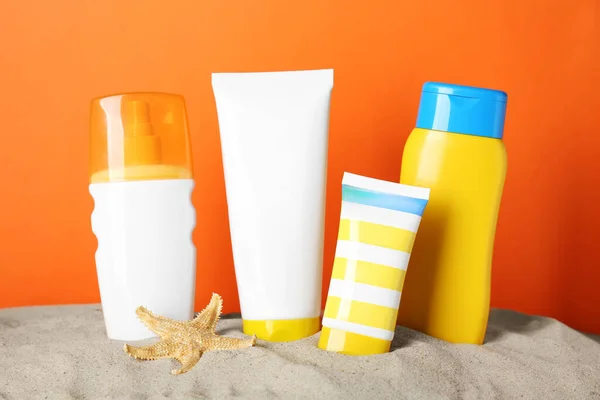 stock image Different suntan products and starfish on sand against orange background