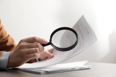 Kadın masadaki büyüteçle belgeye bakıyor, yakın plan. Konsept aranıyor