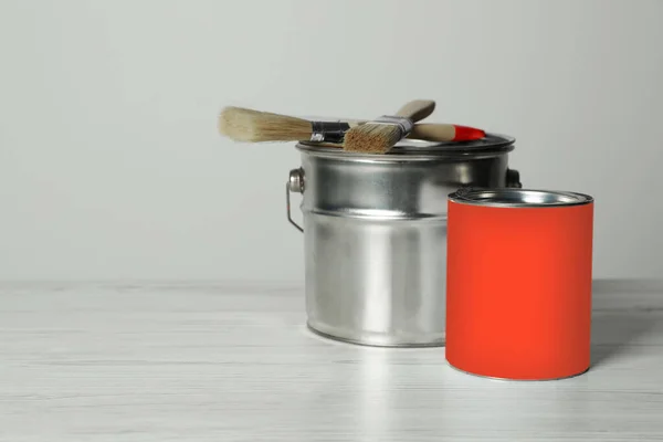Can of orange paint, bucket and brushes on white wooden table. Space for text