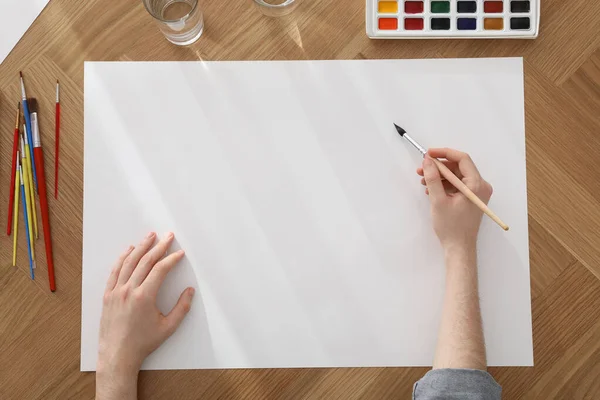 Man Schilderen Met Aquarel Blanco Papier Aan Houten Tafel Bovenaanzicht — Stockfoto
