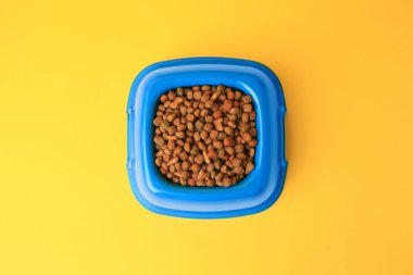 Sarı arka planda besleme kabında kuru hayvan mamaları, üst manzara.