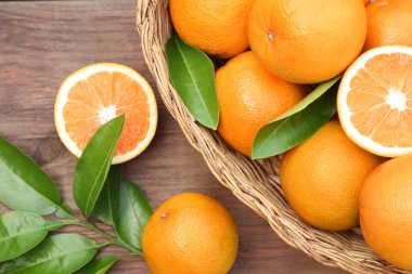 Hasır sepet, olgun sulu portakallar ve ahşap masada yeşil yapraklar.