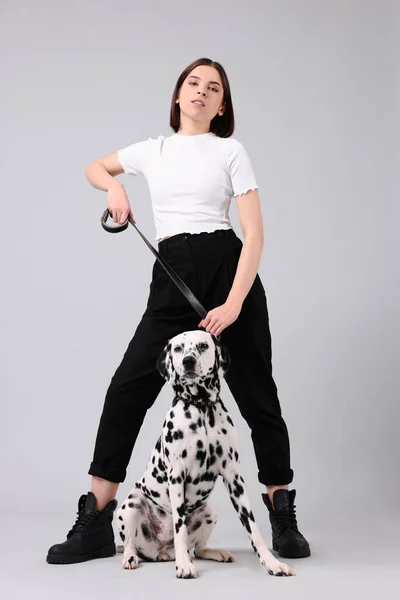 ライトグレーの背景に彼女の愛らしいダルマチアの犬と美しい若い女性 可愛いペット — ストック写真