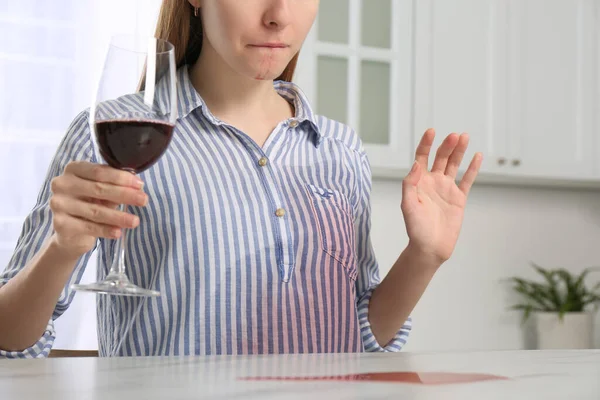 Woman with wine stain on her shirt at white marble table indoors, closeup
