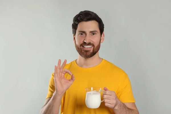 Snygg Man Med Läcker Yoghurt Visar Gest Ljusgrå Bakgrund — Stockfoto