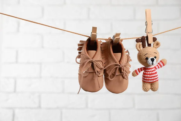 Cute baby shoes and crochet toy drying on washing line against white brick wall. Space for text