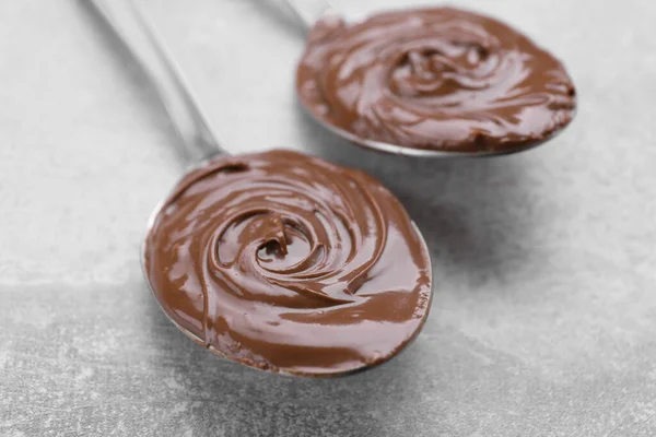 Spoons with chocolate paste on grey textured table, closeup