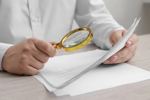 Man looking at document through magnifier at white wooden table, closeup. Searching concept