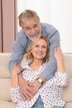 Evdeki koltukta kucaklaşan mutlu, olgun bir çift. Randevu ajansı