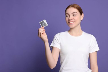 Kadın mor arka planda prezervatif tutuyor, mesaj için yer var. Güvenli seks.