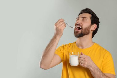 Yakışıklı adam açık gri arka planda lezzetli yoğurt yiyor. Metin için boşluk