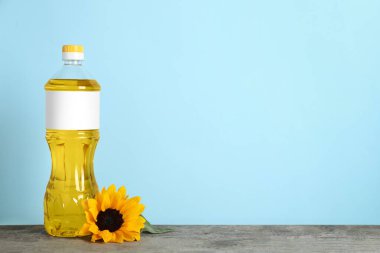 Bottle of cooking oil and sunflower on wooden table, space for text