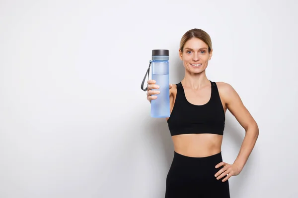 ライトグレーの背景に水のボトルを持つスポーツ女性 テキストのためのスペース — ストック写真