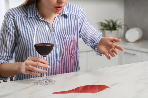 Embarrassed woman with wine stain on her shirt and spilled wine at white marble table indoors, closeup