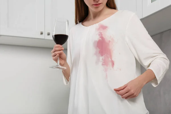 Woman with stain on her clothes and glass of wine indoors, closeup