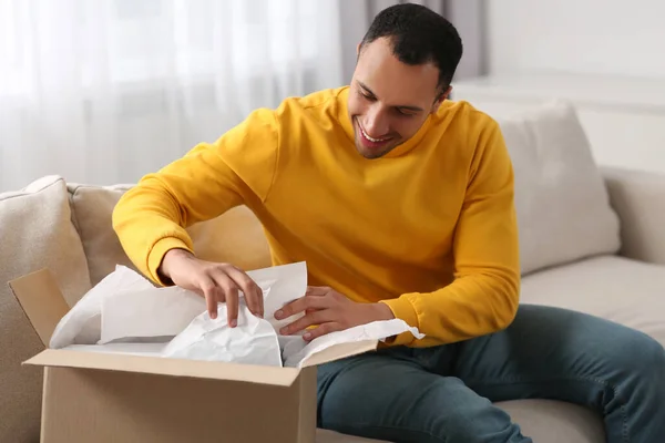 Happy young man opening parcel at home. Internet shopping
