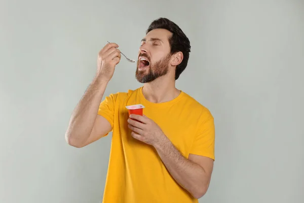一个英俊的男人在浅灰的背景下吃美味的酸奶 — 图库照片