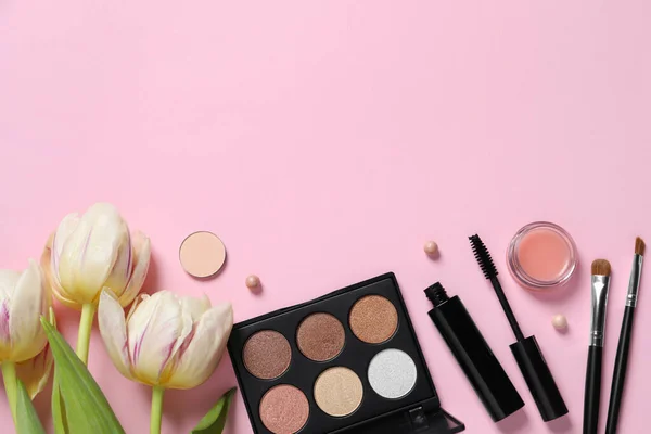 Flat lay composition with different makeup products and beautiful tulips on pink background. Space for text