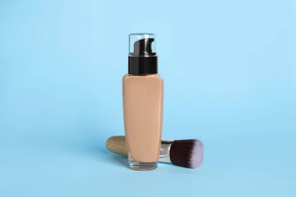 Bottle of skin foundation and brush on light blue background. Makeup product